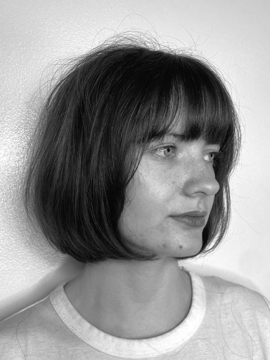 Black-and-white portrait of a woman with a short bob haircut, viewed in profile to the right, against a plain wall.
