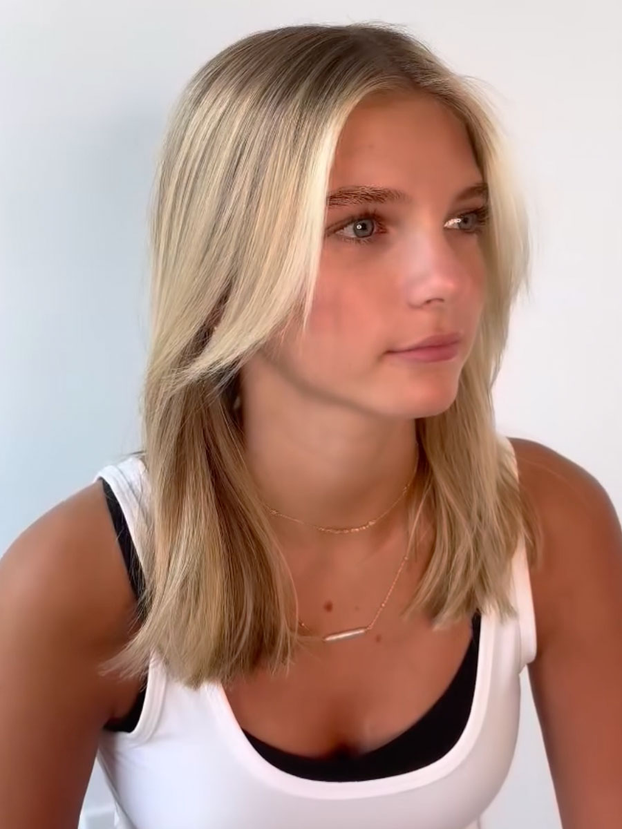 Young woman with shoulder-length blonde hair, wearing a white tank top, looking to the right against a light background.