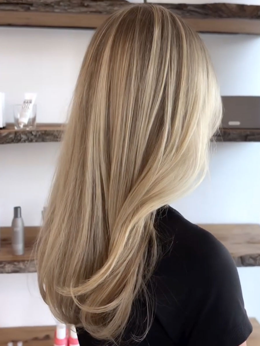 Side view of a woman with long, layered blonde hair in a salon setting.