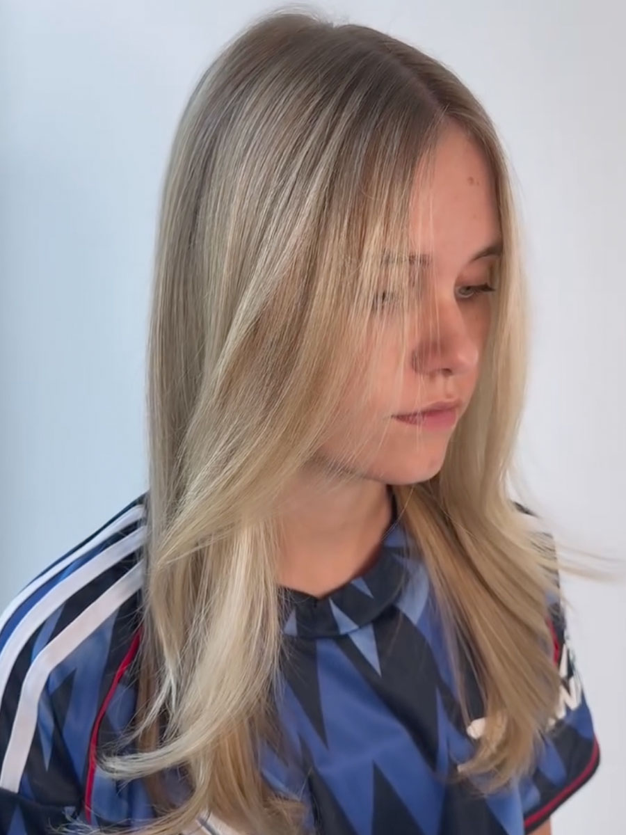 Young woman with straight, shoulder-length blonde hair looking downward, wearing a blue geometric-patterned shirt.