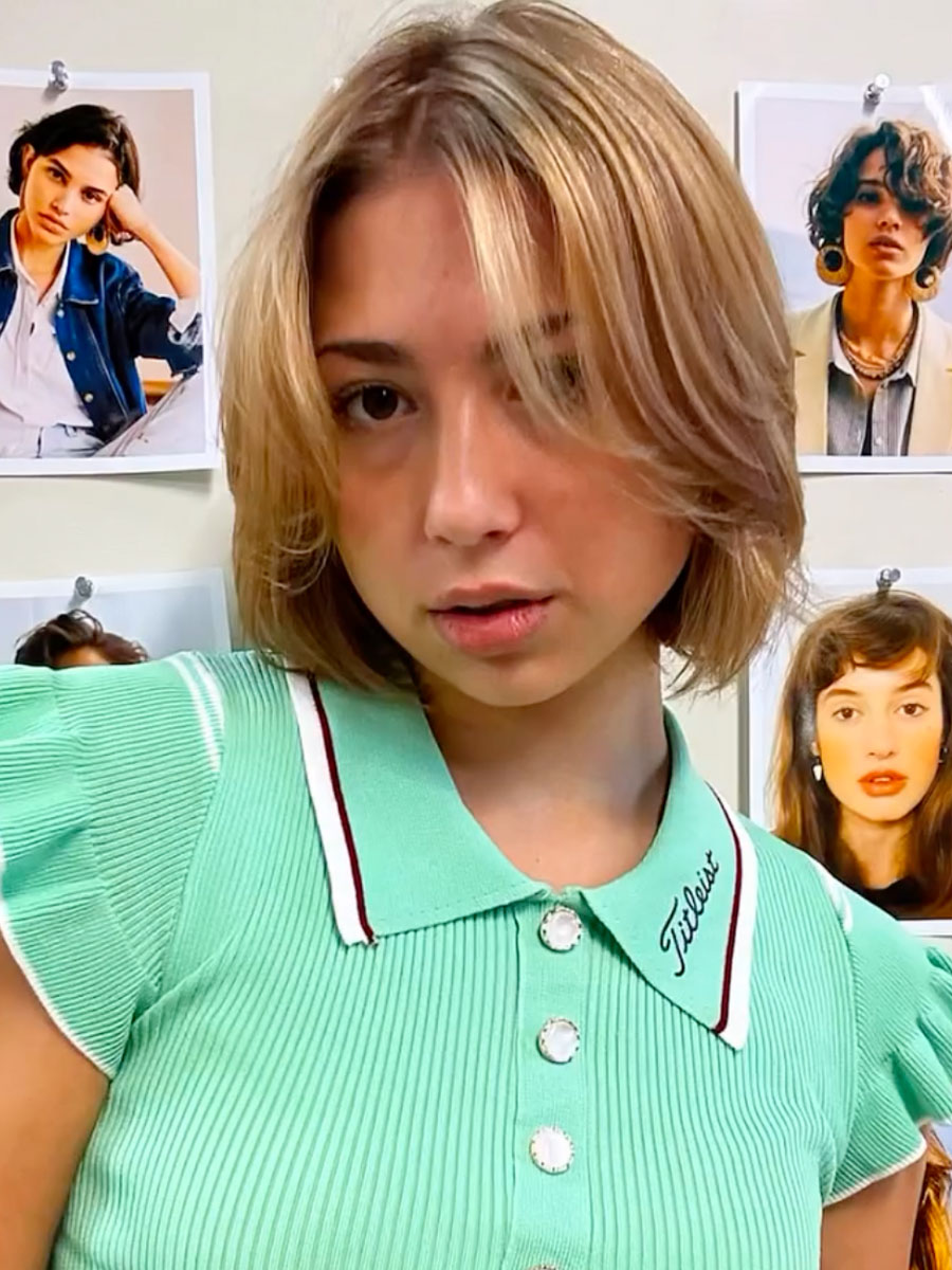 Young woman with short light brown hair wearing a mint green polo with a Titleist collar, looking at the camera, fashion photos on the wall behind.