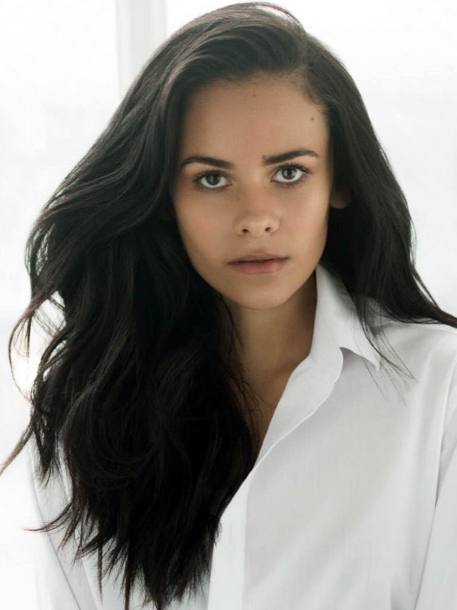 Portrait of a young woman with long dark hair in a white shirt, looking straight at the camera.