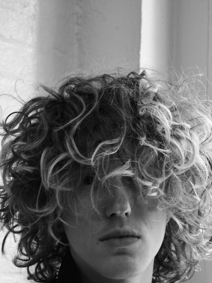 Person with curly hair obscuring their face, looking slightly downward (black-and-white portrait).