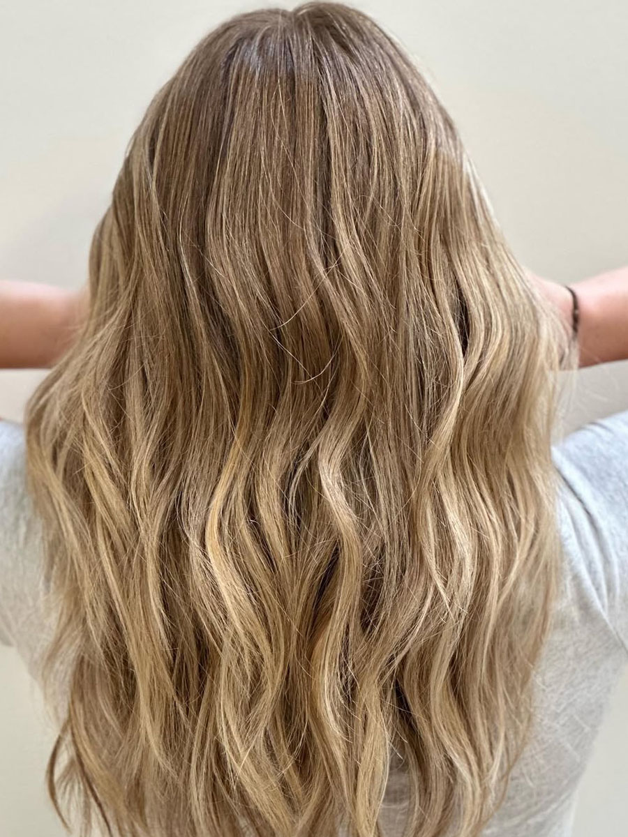 Back view of a person with long, wavy blonde hair cascading down their back.