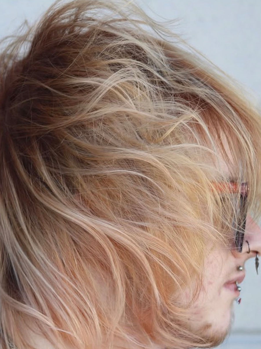 Side profile of a person with long blonde hair blown across their face by the wind.